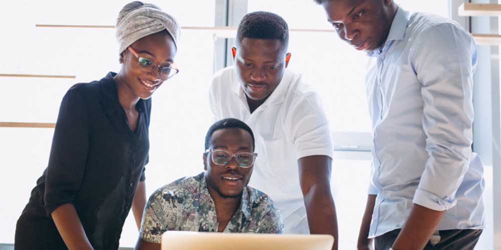 Four Black professionals around a laptop, symbolizing economic inclusivity in Black Business Month