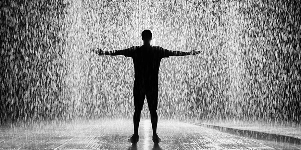 A black-and-white image of a man standing in the rain shows Rangam's resilient journey through testing times