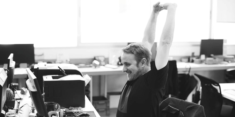 Monochrome image of a man stretching his arm while working in the office