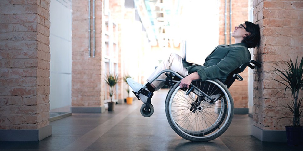 A woman in a wheelchair, leaning against a wall, reflects weariness toward the rising workplace disability discrimination